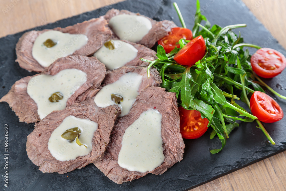 boiled beef tongue with sauce, capers and greens on a black granite tile boiled beef tongue with sauce, capers and greens on a black granite tile