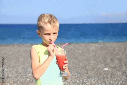 Little boy drinking water-melon juice at hot summer day on beach