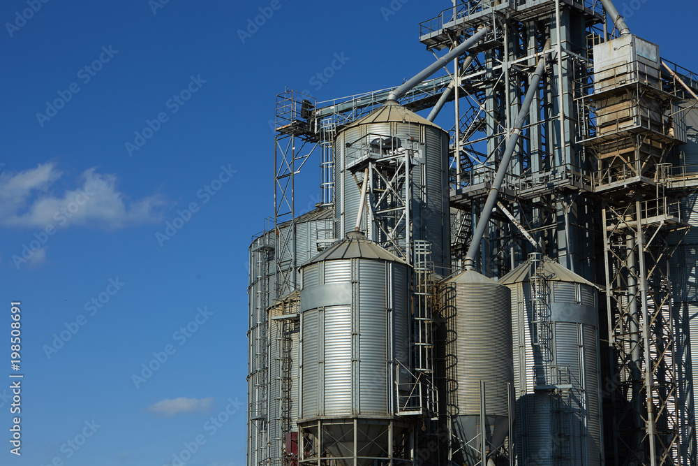 Modern grain terminal. Metal tanks of elevator. Grain-drying complex construction. Commercial grain or seed silos at seaport. Steel storage for agricultural harvest.