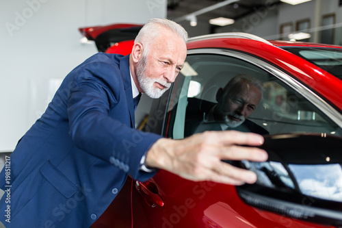 Senior man choosing a new car at car showroom.