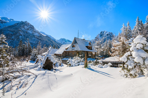 Small wooden house in winter landscape near Morskie Oko lake with sun on blue sky, Tatra Mountains, Poland
