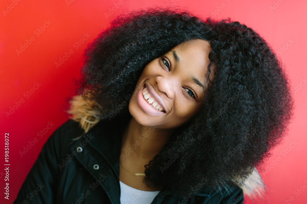 Young beautiful African American girl in a black coat smiling on red background Young beautiful African American girl in a black coat smiling on red background