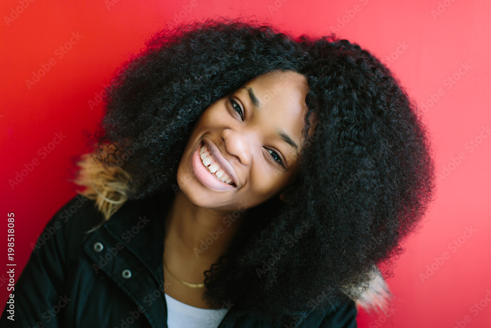 Young beautiful African American girl in a black coat smiling on red background Young beautiful African American girl in a black coat smiling on red background