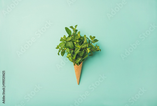Flat-lay of sweet waffle ice-cream cone with bunch of fresh green mint over pastel mint background, top view. Spring or summer mood concept