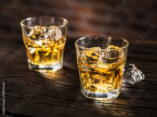 Whiskey glasses or glasses of whiskey with ice cubes on the wooden table.