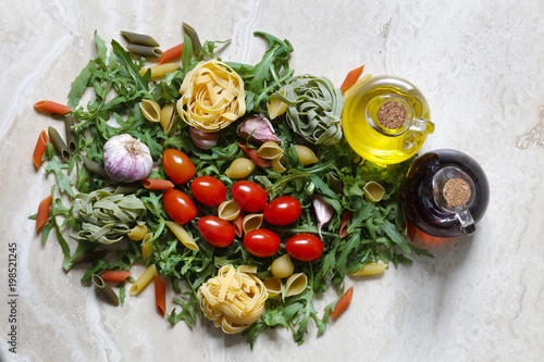 Rocket Arugula with plum tomatoes and garlic with Tagliatelle and penne pasta tricolore ingredients for Italian food on marble table with olive oil