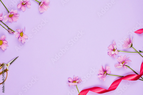 Flatlay frame arrangement with violet daises, scissors and ribbon, violet background, copyspace