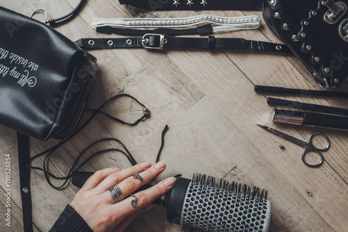 black colors a female hand in rings holds a hairbrush next to a cosmetic bag with eyebrow pencils and eyes on a wooden background view from above
