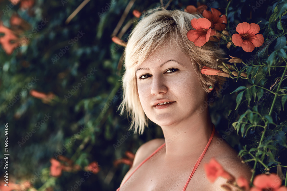 Beautiful blonde woman portrait with the orange flowers of the trumpet vine bloom. Orange flowers of the trumpet vine or trumpet creeper (Campsis radicans), also known as 