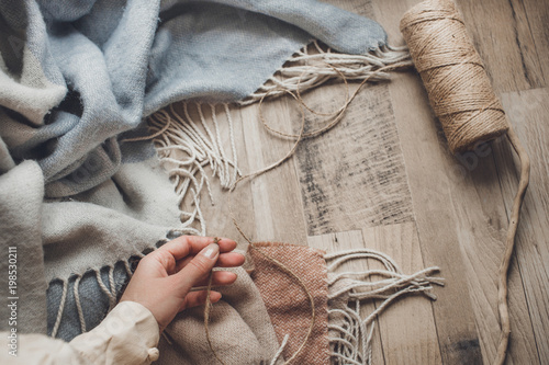 pastel colors female hand in rings holds the twine on a woolen blue scarf which rests on a wooden background