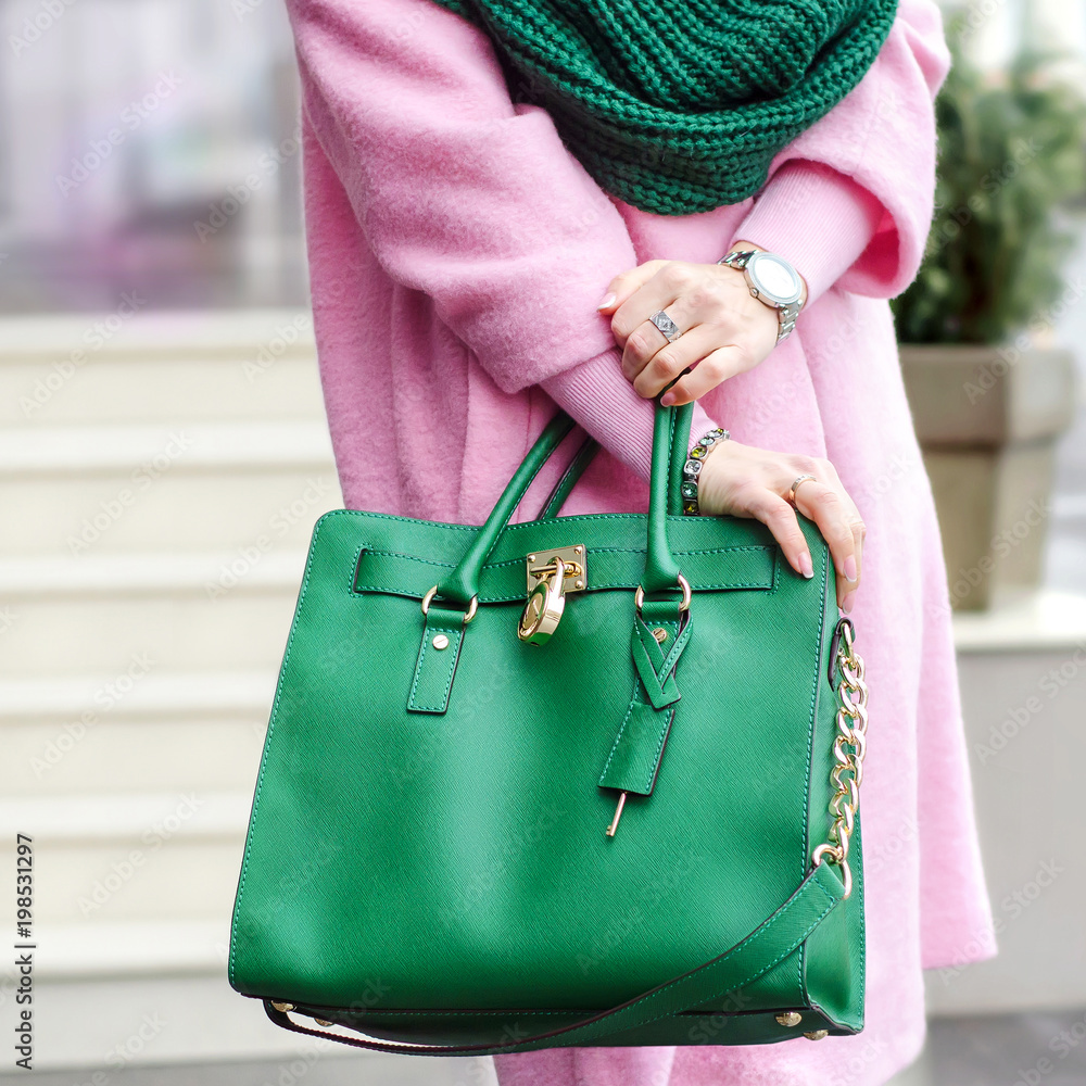 Bag in female hands. Bright leather bag. accessories. Pink coat and green  bag. Stock Photo