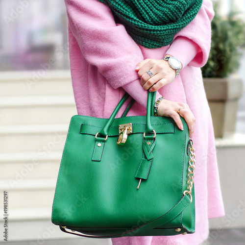 Bag in female hands. Bright leather bag. accessories. Pink coat and green bag. 