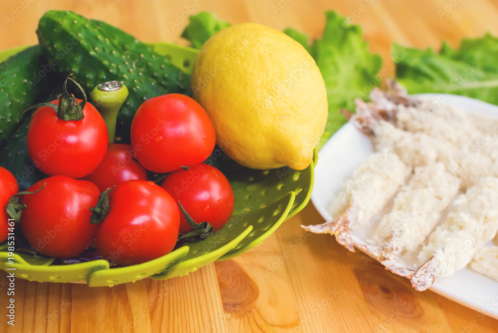 Raw shrimp in batter ready for roasting next to a basket of cucumber lemon cucumbers and tomatoes against the background of lettuce leaves on a wooden table Raw shrimp in batter ready for roasting next to a basket of cucumber lemon cucumbers and tomatoes against the background of lettuce leaves on a wooden table