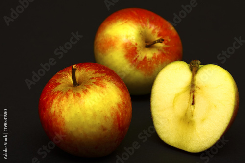 Two whole red apples and one sliced in half isolated on a black background