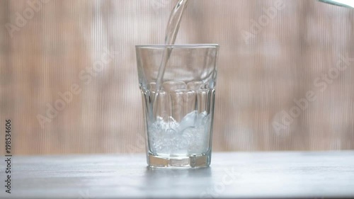 Pouring fresh cold fizzy water into drinking glass on the table, ungraded flat style footage photo