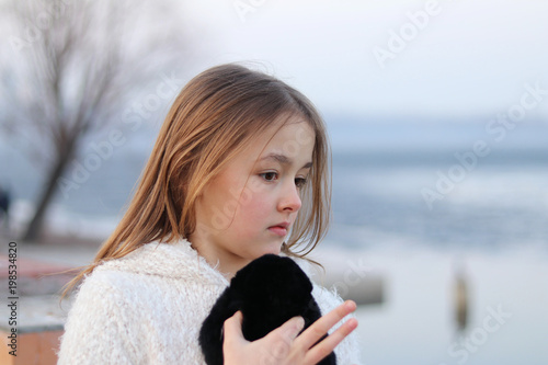 Pretty little pensive girl looking thoughfully to the right holding her soft toy and counting on her fingers, close up, outdoors photo