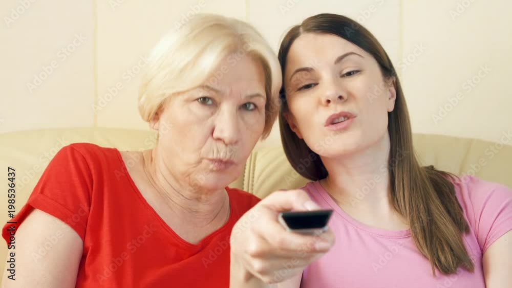 Mother and her young daughter relaxing on sofa at home. Happy family enjoying time together watching TV. Switching channels with remote control Mother and her young daughter relaxing on sofa at home. Happy family enjoying time together watching TV. Switching channels with remote control