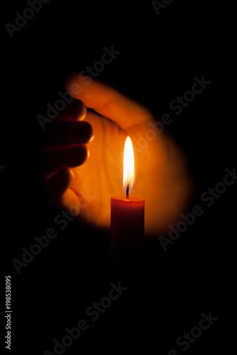 A burning candle at night, surrounded by the hands of a woman. Candle flame glowing on a dark background with free space for text. Close up, shallow depth of field.
