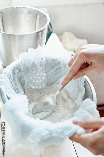 woman preparing vegan almond or coconut milk at home. Pouring the milk into a cheese cloth to filter it. photo