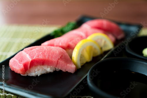 Otoro tuna sushi on black plate along with Japanese sauce and green leaf decoration, Japanese food, close up at sushi ..
