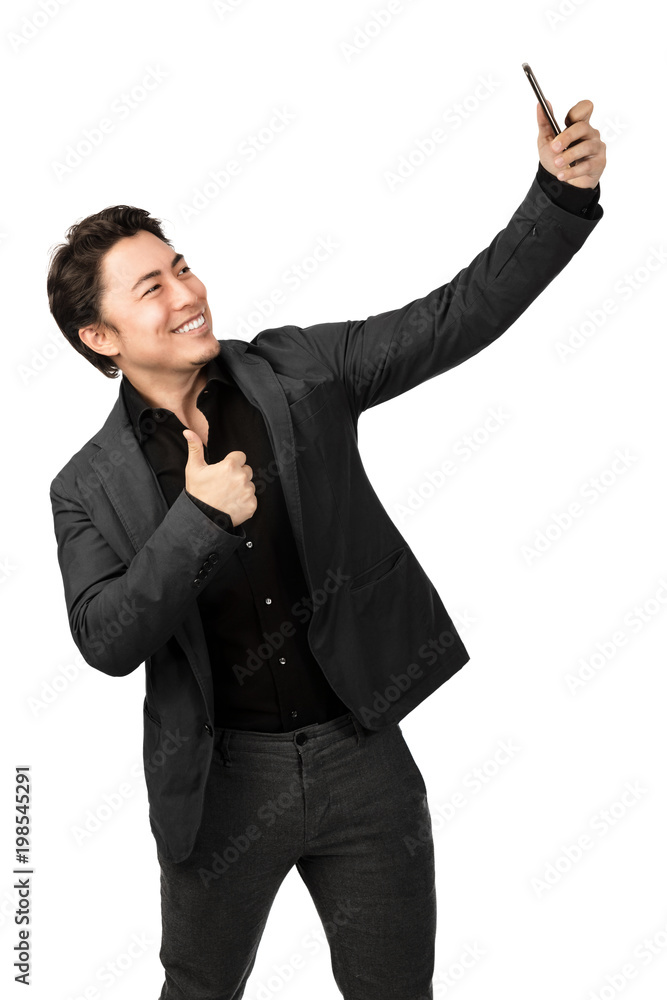 Smiling happy man taking a selfie with his phone and doing thumbs up. White background. Smiling happy man taking a selfie with his phone and doing thumbs up. White background.