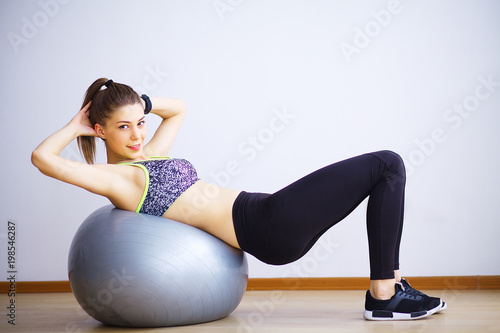 Young woman practicing yoga, doing Wild Thing, Flip-the-Dog exercise, Camatkarasana pose, working out, wearing sportswear, black pants and top, indoor full length, gray wall in yoga studio