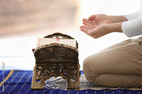 Fototapeta Naklejka Na Ścianę i Meble -  Young Muslim man praying on rug against blurred background