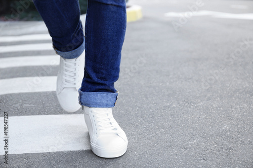 Stylish man in white shoes walking across the city street