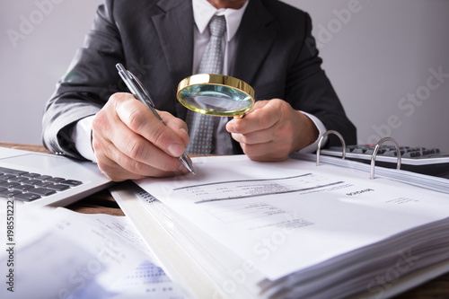 Businessperson Looking At Receipts Through Magnifying Glass