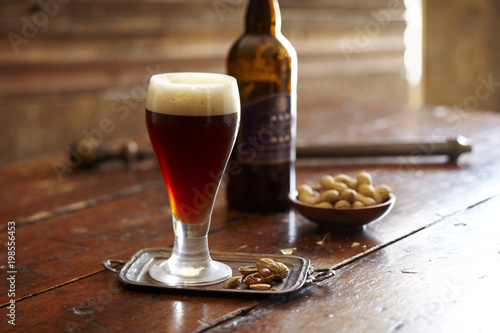 Glass of cold beer with peanuts on table