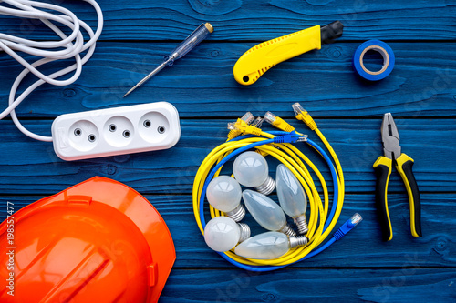 Electrician work concept. Hard hat, tools, cabel, bulb, socket outlet on blue wooden background top view