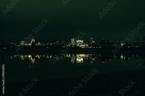 Night city view with lots of lights and its reflection in a river water