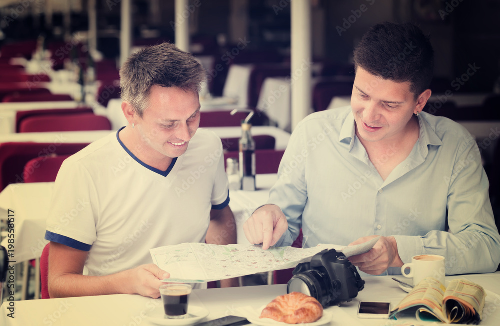 Fototapeta premium two friendly men sitting with coffee and looking at map in cafe