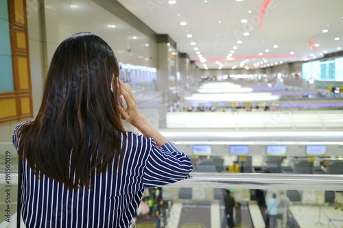 asian woman use mobile phone and stand alone at Don Mueang international airport Bangkok, Thailand. Transportation and people concept. Selective focus with blurred background. photo