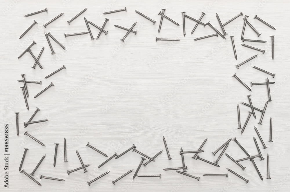 Frame made of scattered nails on white wooden board surface background with copy space. Construction concept background. Frame made of scattered nails on white wooden board surface background with copy space. Construction concept background.