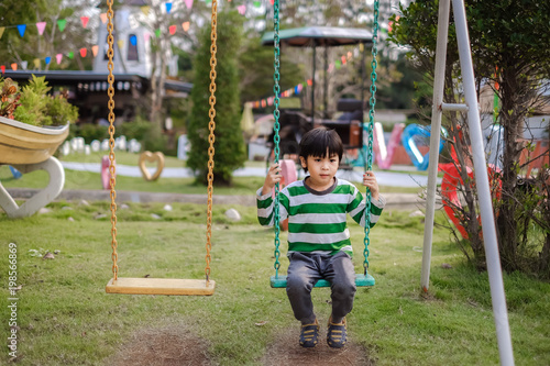 A cute boy playing a swing in the playground.
