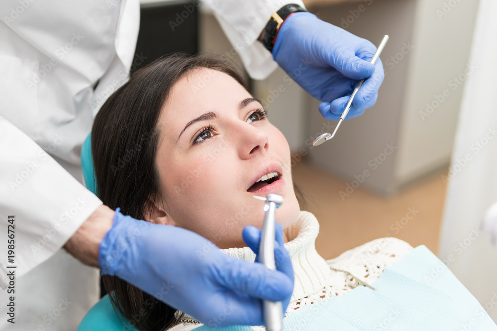 Fototapeta premium Female patient sitting in a dentist's chair opened her mouth to drill a tooth
