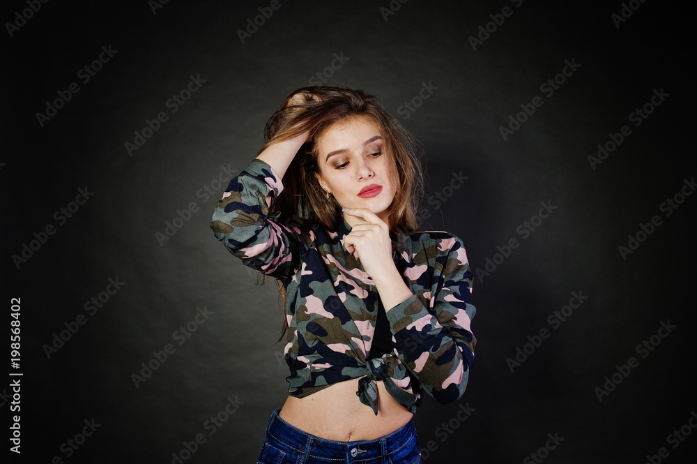 Handsome brunette girl wear military shirt and jeans, posing at studio against gray background. Studio model portrait. Handsome brunette girl wear military shirt and jeans, posing at studio against gray background. Studio model portrait.