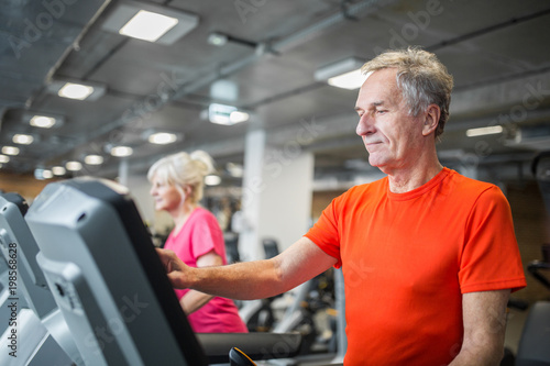 Senior man touching screen of treadmill at gym