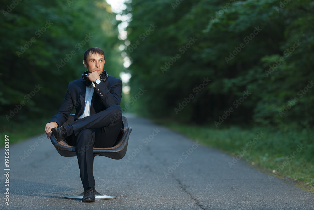 Young business man sitting on chair in suit and headphones in forest Young business man sitting on chair in suit and headphones in forest