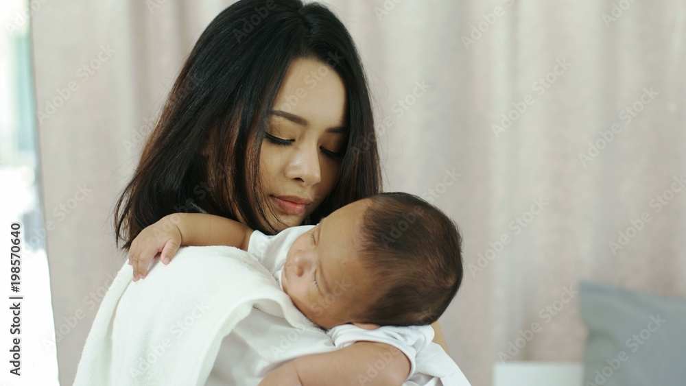 Young beautiful Asian mother caring and playing with her baby in the bedroom on a bright morning sunshine Young beautiful Asian mother caring and playing with her baby in the bedroom on a bright morning sunshine