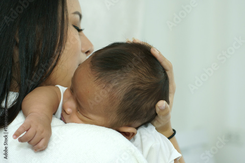 Young beautiful Asian mother caring and playing with her baby in the bedroom on a bright morning sunshine