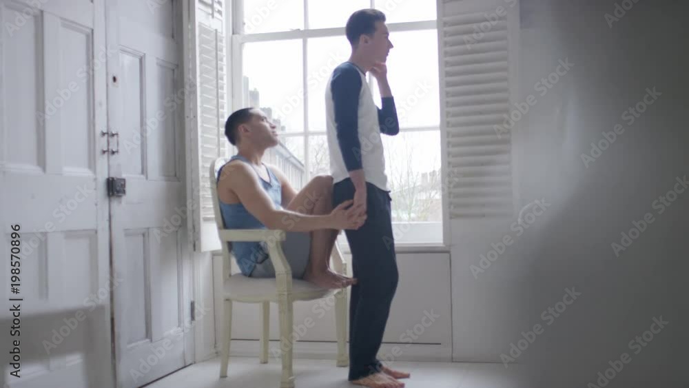 Male couple relaxing in front of their apartment window Male couple relaxing in front of their apartment window