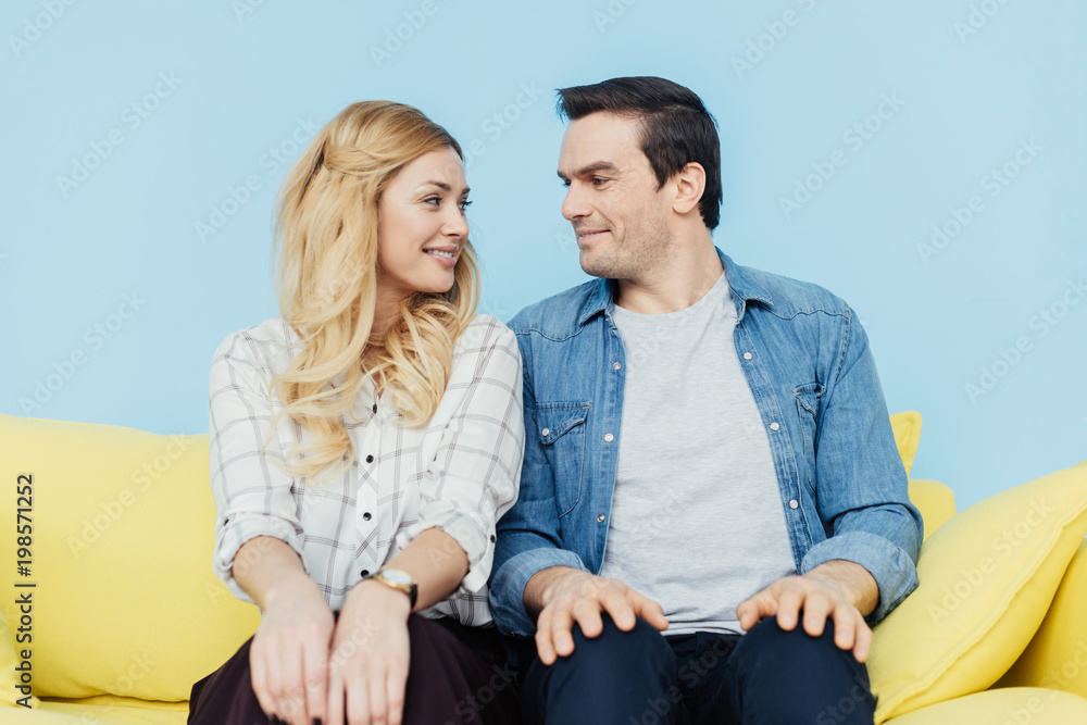 Pretty couple looking at each other and sitting on yellow sofa Pretty couple looking at each other and sitting on yellow sofa