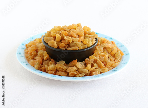 Raisins or dry grapes, organic type, healthy vegetarian food, in a bowl on a plate with spilled raisins.