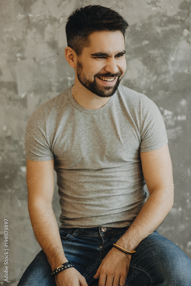 Obraz premium Portrait shot of handsome young man with a beard looking and smiling into the camera on a gray background.