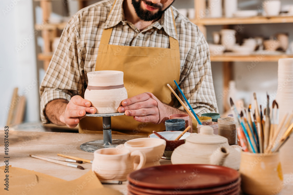 cropped view of man painting ceramic dishware in pottery workshop