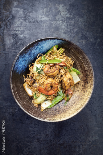 Traditional stir-fried Thai phat mama mie noodles with king prawns and vegetables as top view in a bowl