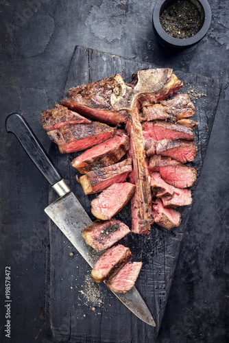 Barbecue dry aged wagyu porterhouse steak sliced as top view with smoked pepper on a burnt board