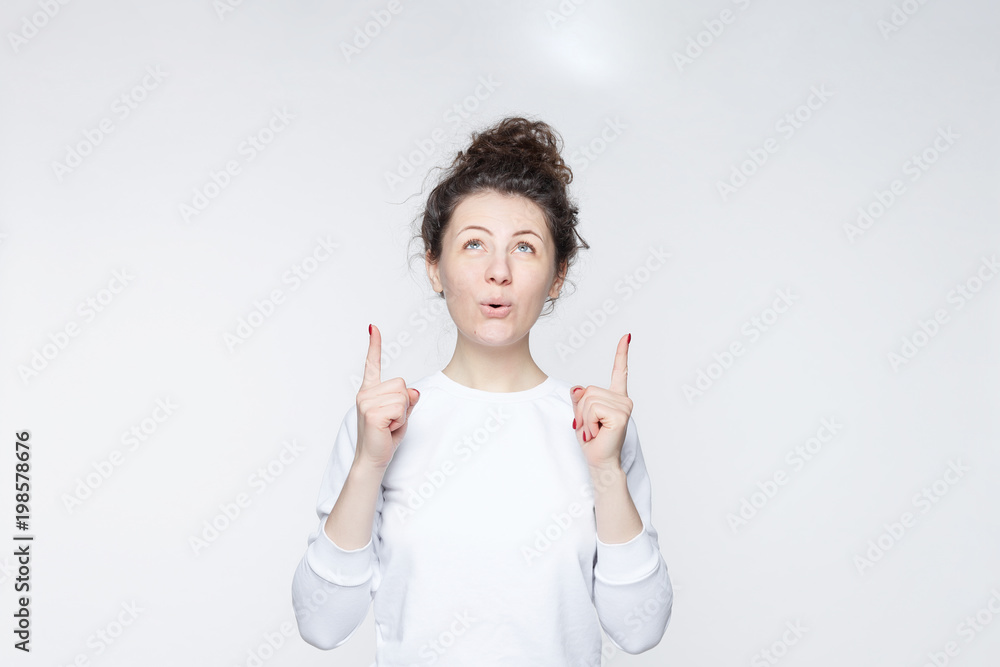 Portrait of happy smiling woman points with both hands up, advertises something as stands against white copy space. Cheerful young female model indicates with fore fingers. Advertising concept. Portrait of happy smiling woman points with both hands up, advertises something as stands against white copy space. Cheerful young female model indicates with fore fingers. Advertising concept.